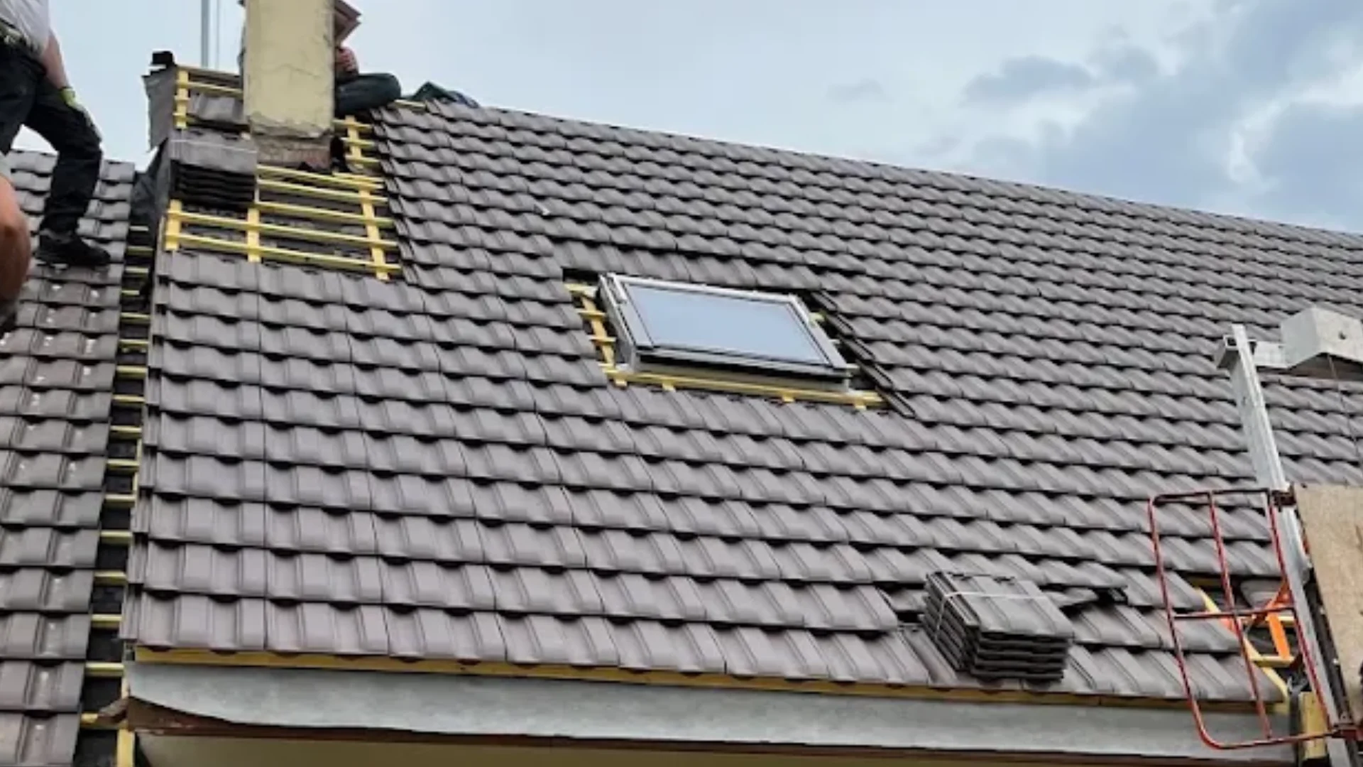 Couvreur zingueur au travail sur une toiture en tuile, châssis de toit et souche de cheminée